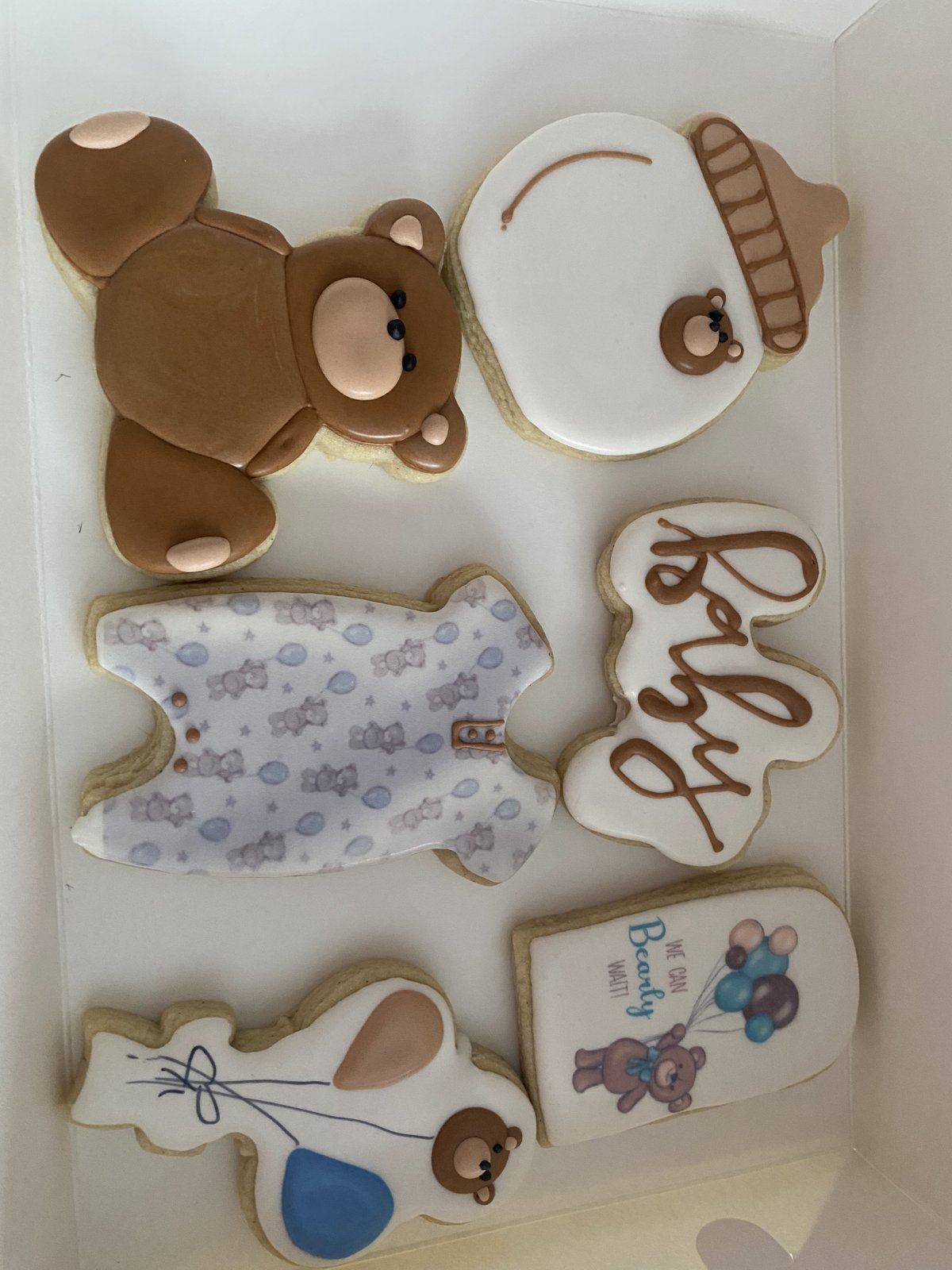 Decorated baby shower cookies: a teddy bear, a baby onesie, a rattle, a baby bottle, and a Baby script cookie.