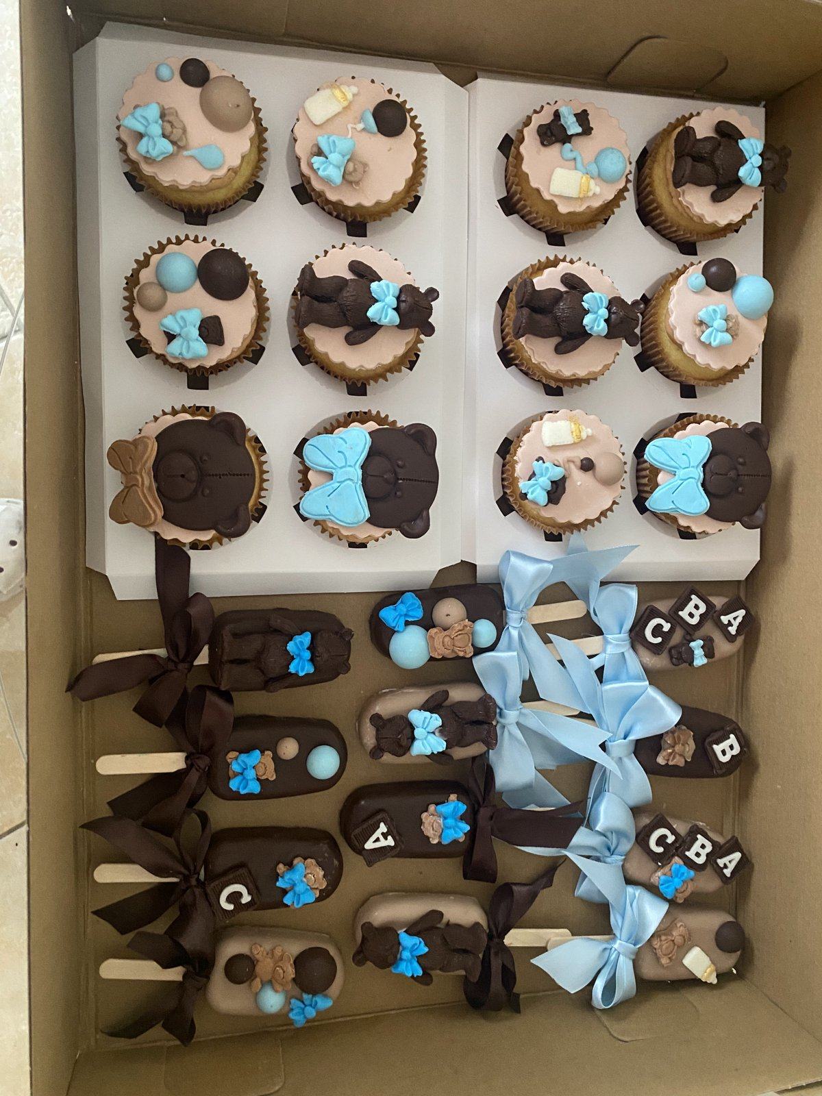 Baby shower treat box with cupcakes, chocolate cakesicles, and teddy bear and ABC block decorations in blue and brown.
