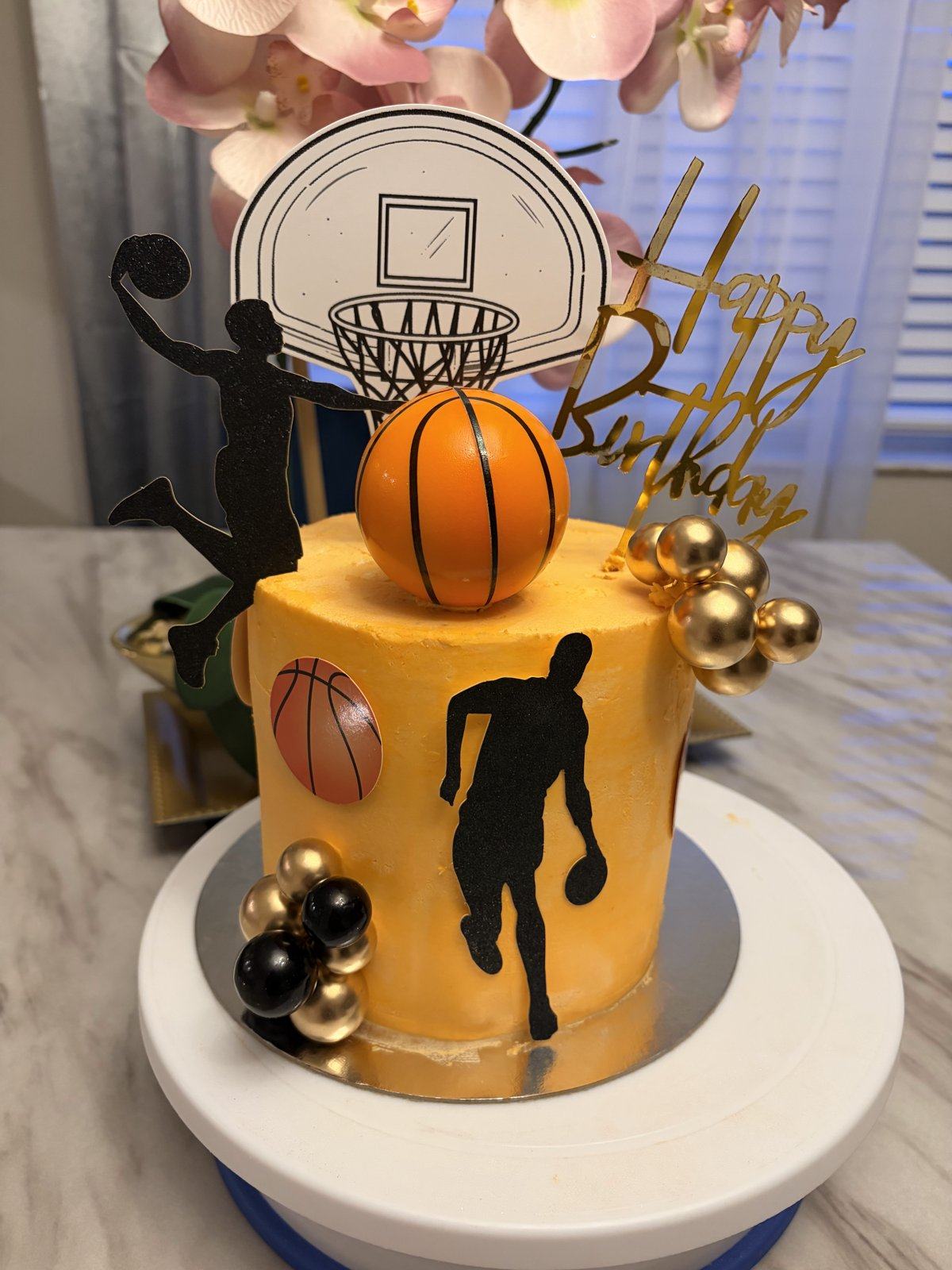 Yellow basketball birthday cake with player silhouettes, a hoop topper, a basketball, and gold spheres.
