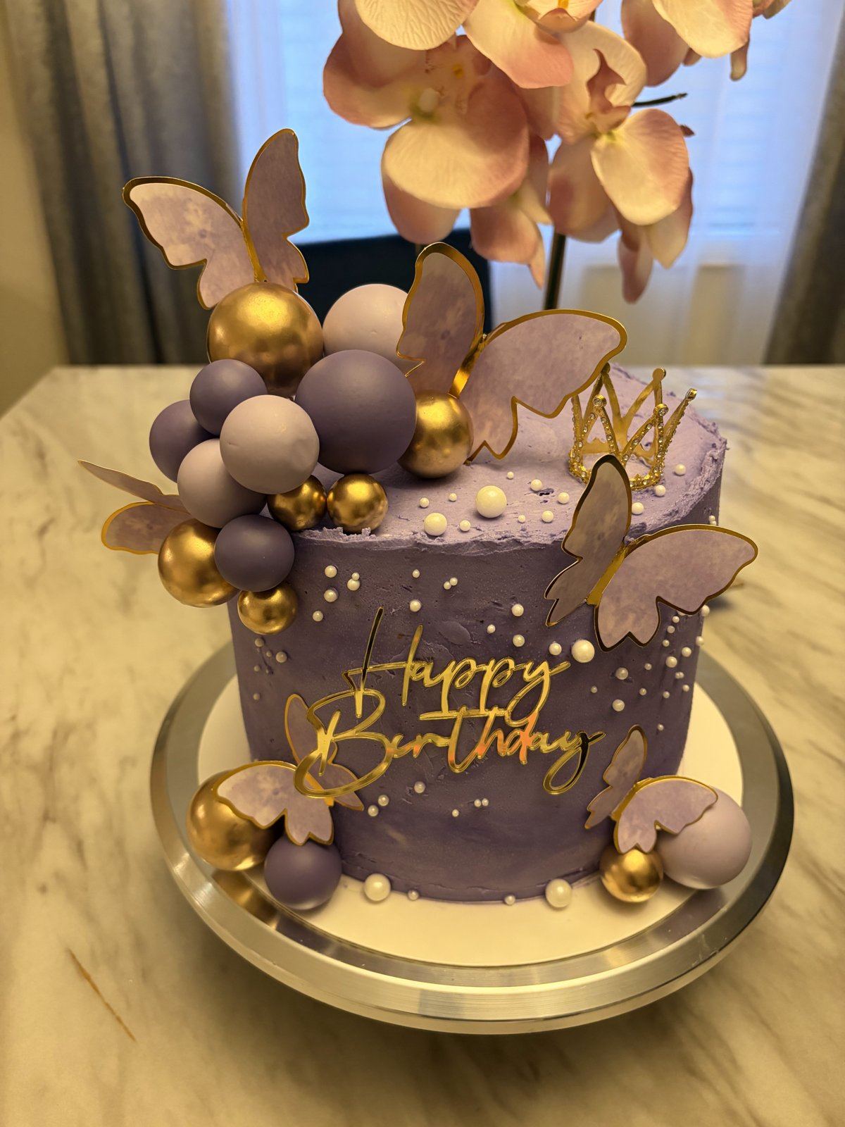 Lavender birthday cake with a gold Happy Birthday topper, lavender and gold spheres, and gold-edged butterflies.