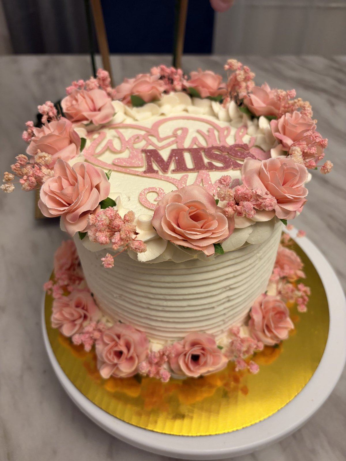 White textured cake ringed with pink buttercream roses and baby’s breath.