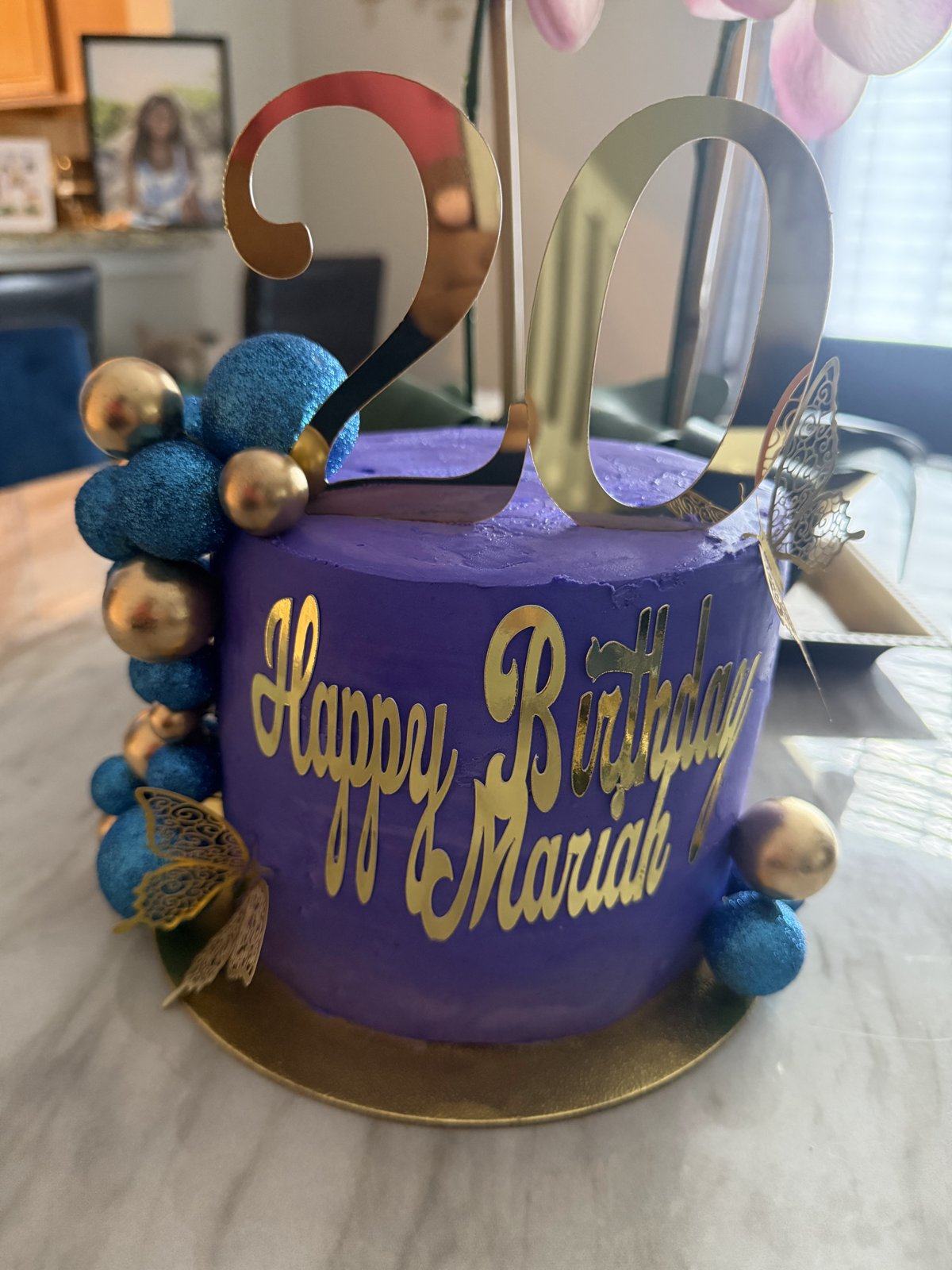 Purple birthday cake with gold Happy Birthday lettering, a large gold 20 topper, and blue and gold spheres.