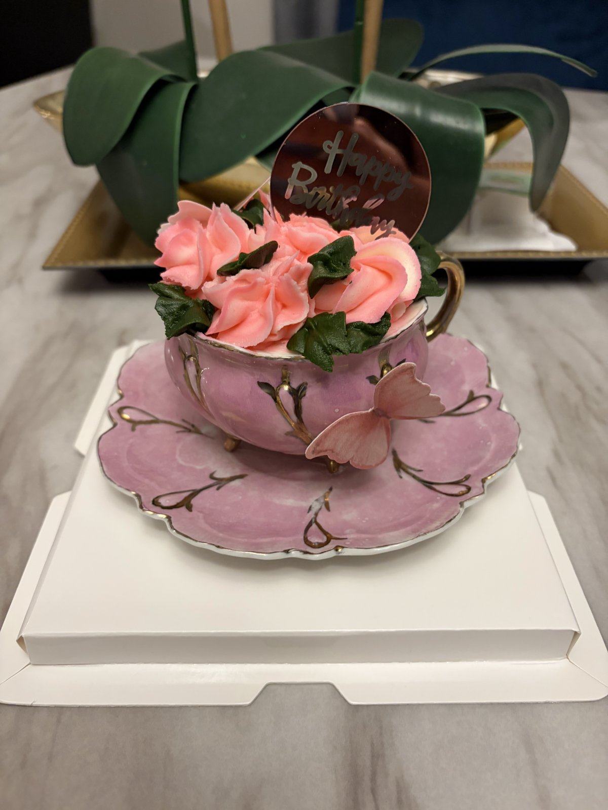 Small cake shaped like a pink teacup on a saucer, filled with pink buttercream roses.