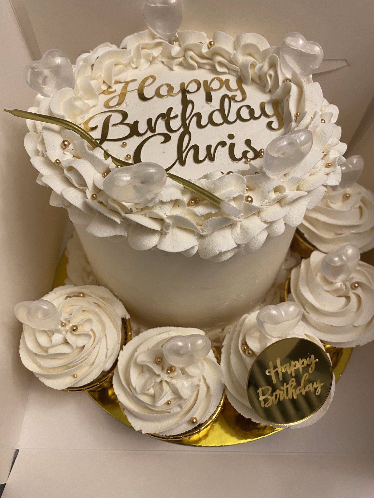 White Happy Birthday cake with piped rosettes and pearls, surrounded by matching white cupcakes.