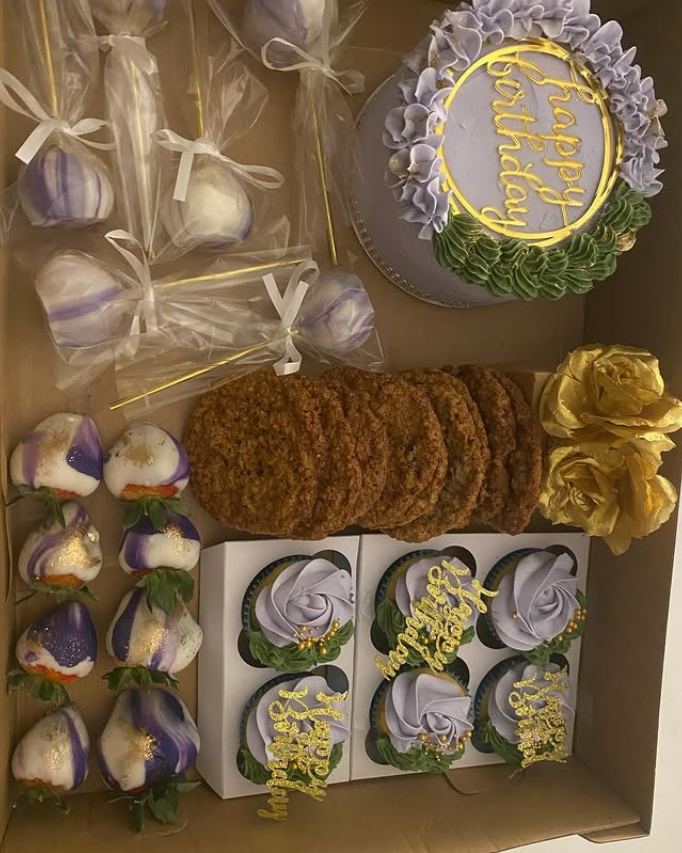Gift box with a lavender mini cake, wrapped cake pops, marbled chocolate-covered strawberries, cookies, and lavender rose cupcakes with gold toppers.