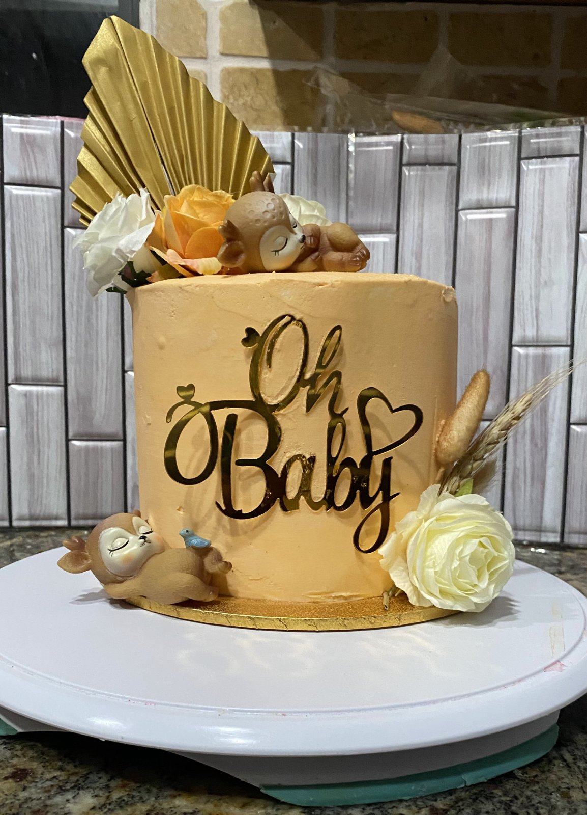 Tan buttercream baby shower cake with gold Oh Baby lettering, a gold fan, cream roses, and small fondant animals.