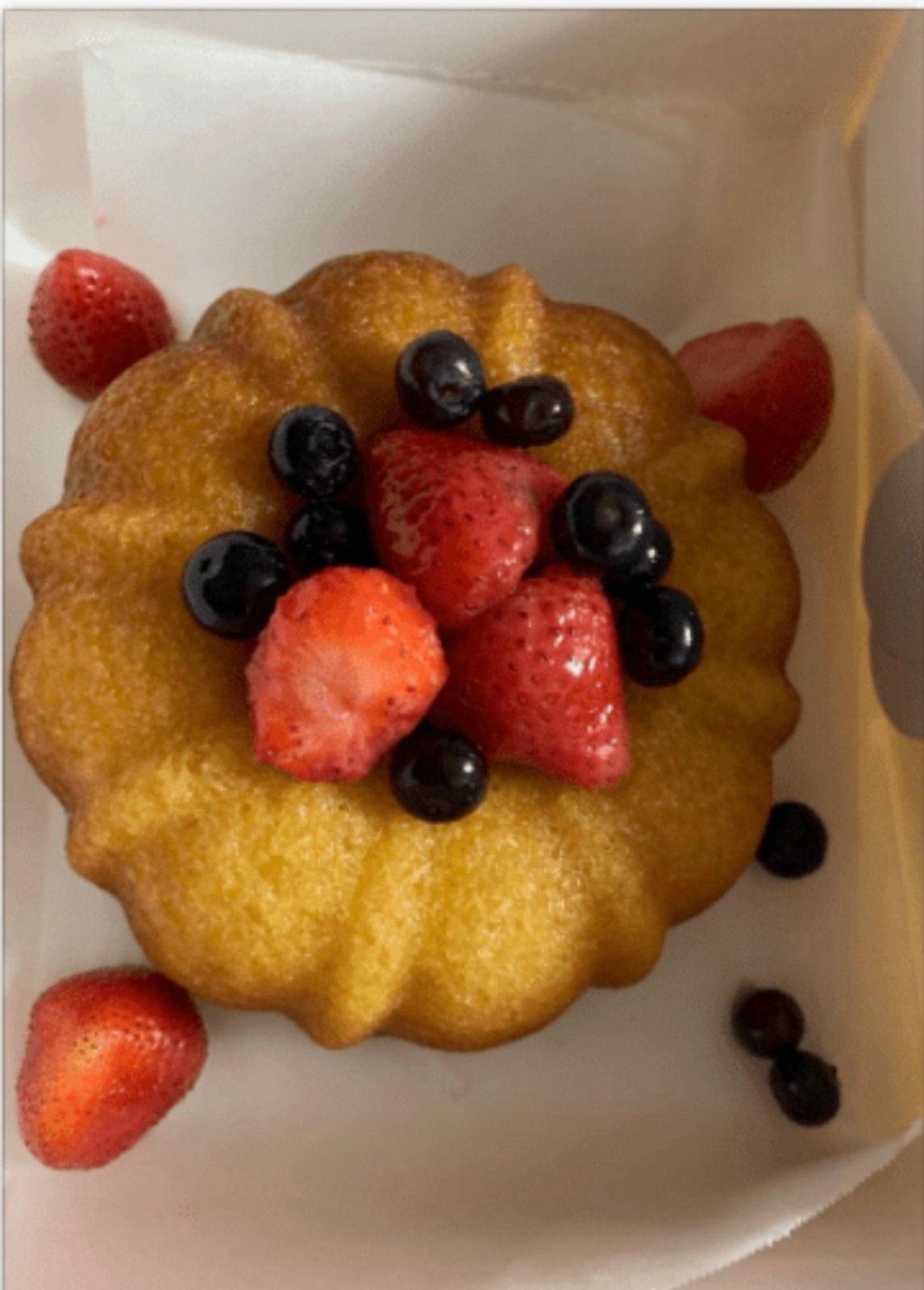 Golden bundt-style rum cake topped with fresh strawberries and blueberries, in a white bakery box.