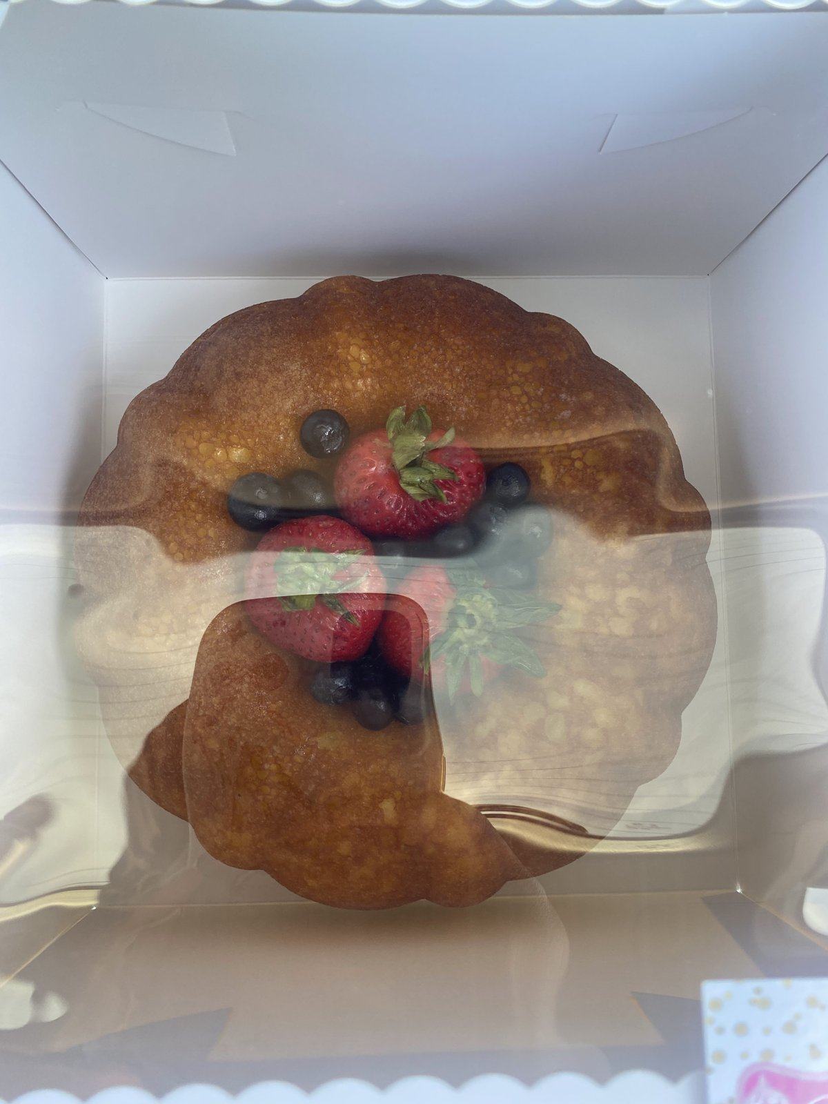 Rum cake topped with berries, packed in a clear-lid bakery box.