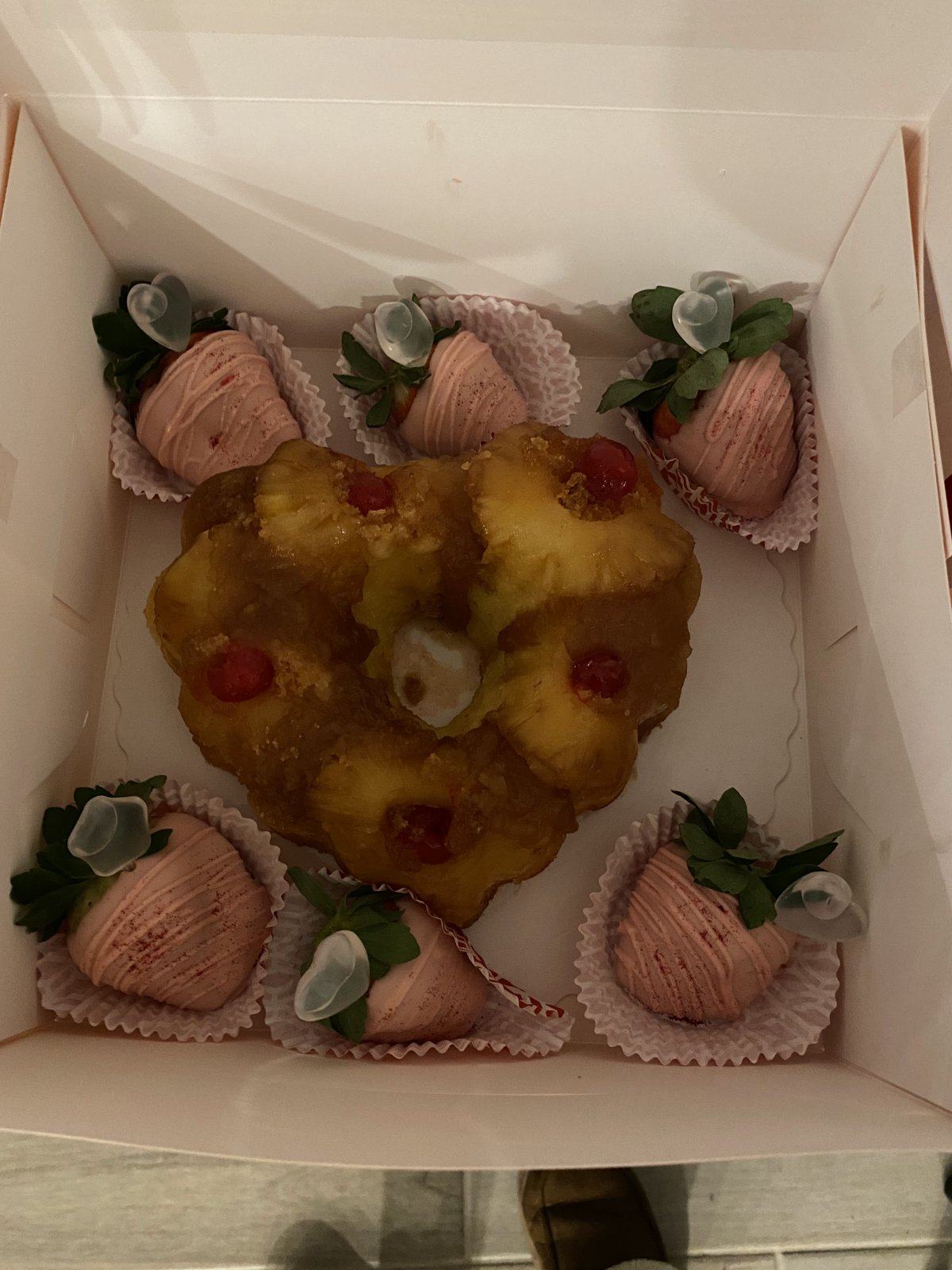 Heart-shaped glazed rum cake in a gift box, surrounded by pink chocolate-dipped strawberries.