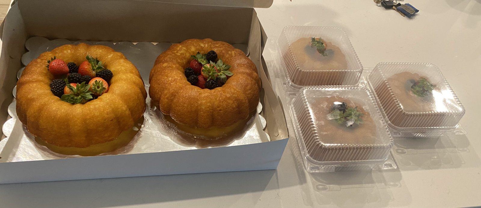 Mini rum cakes, each packed in its own clear container, next to a box of full-size rum cakes.