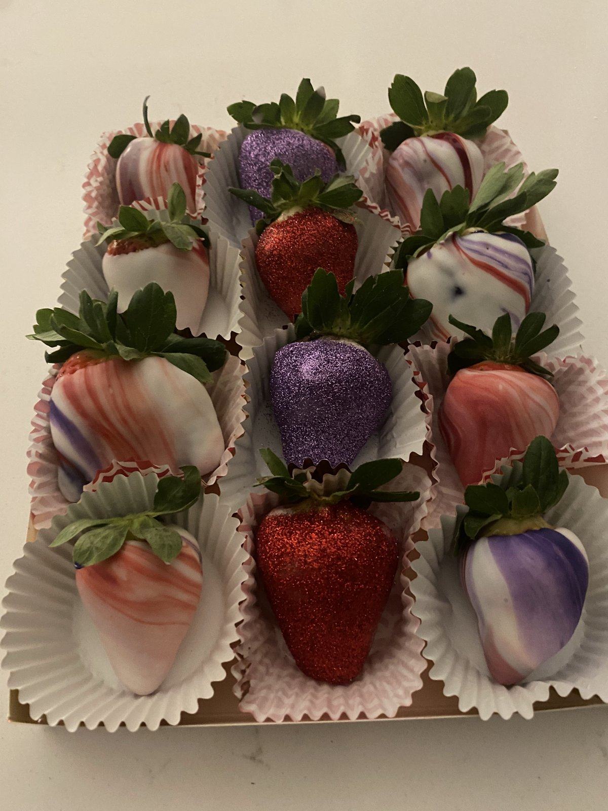 Box of marbled purple, pink, and white chocolate-covered strawberries with glitter.
