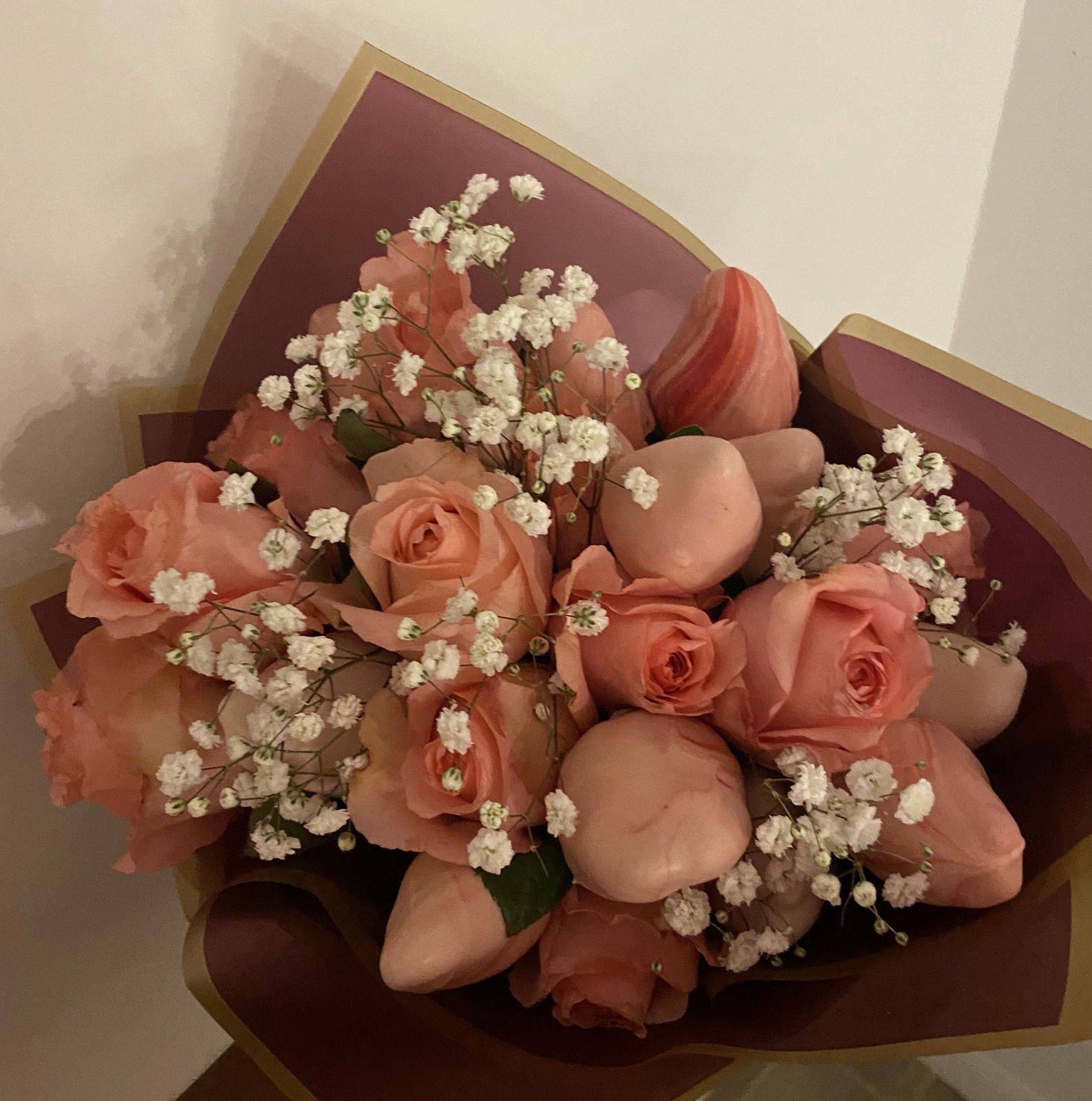 Bouquet of pink chocolate-covered strawberries with peach roses and baby’s breath, wrapped in mauve paper.