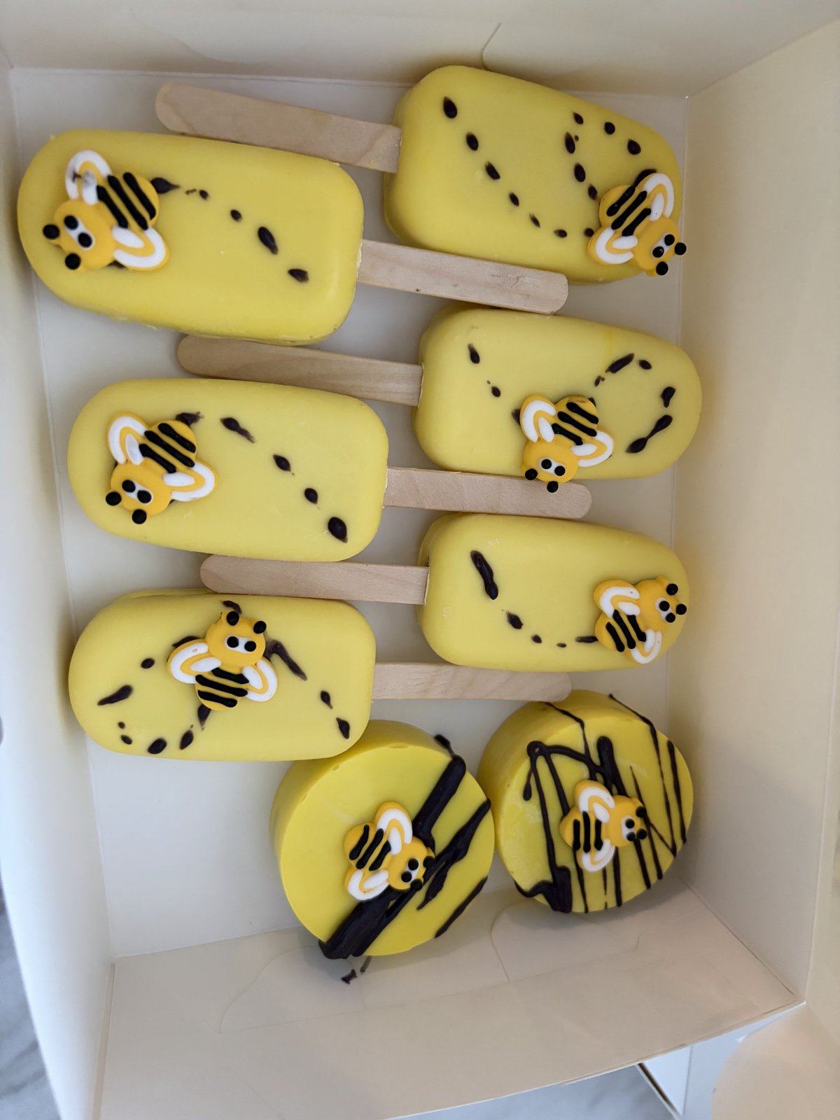 Yellow cakesicles decorated with little bees and dotted flight paths.