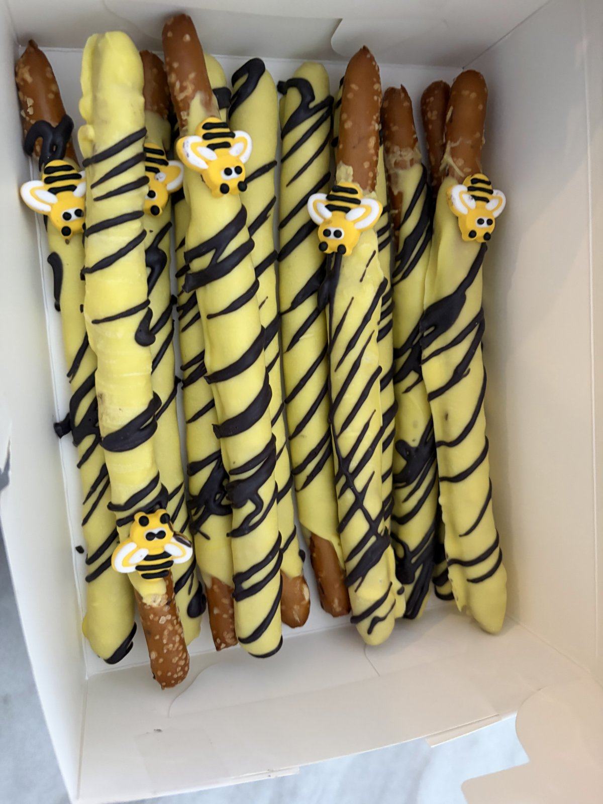 Yellow chocolate-dipped pretzel rods with black drizzle and candy bees.