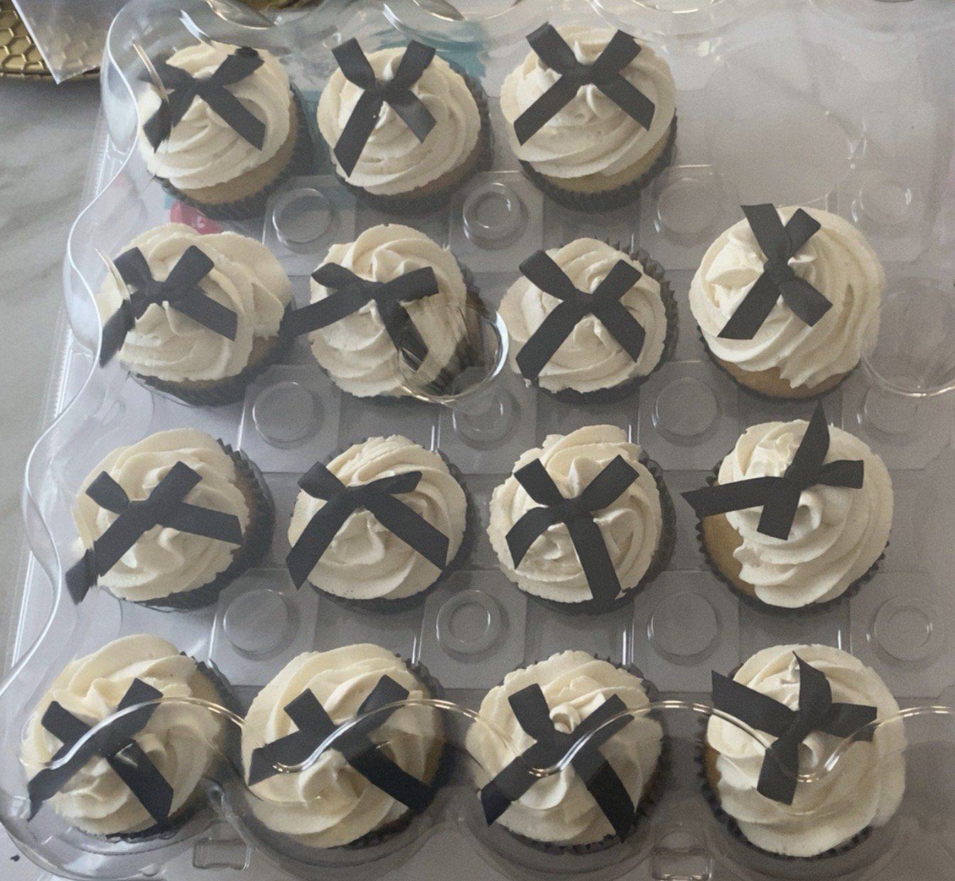 Vanilla cupcakes with white swirled frosting, each topped with a black bow.