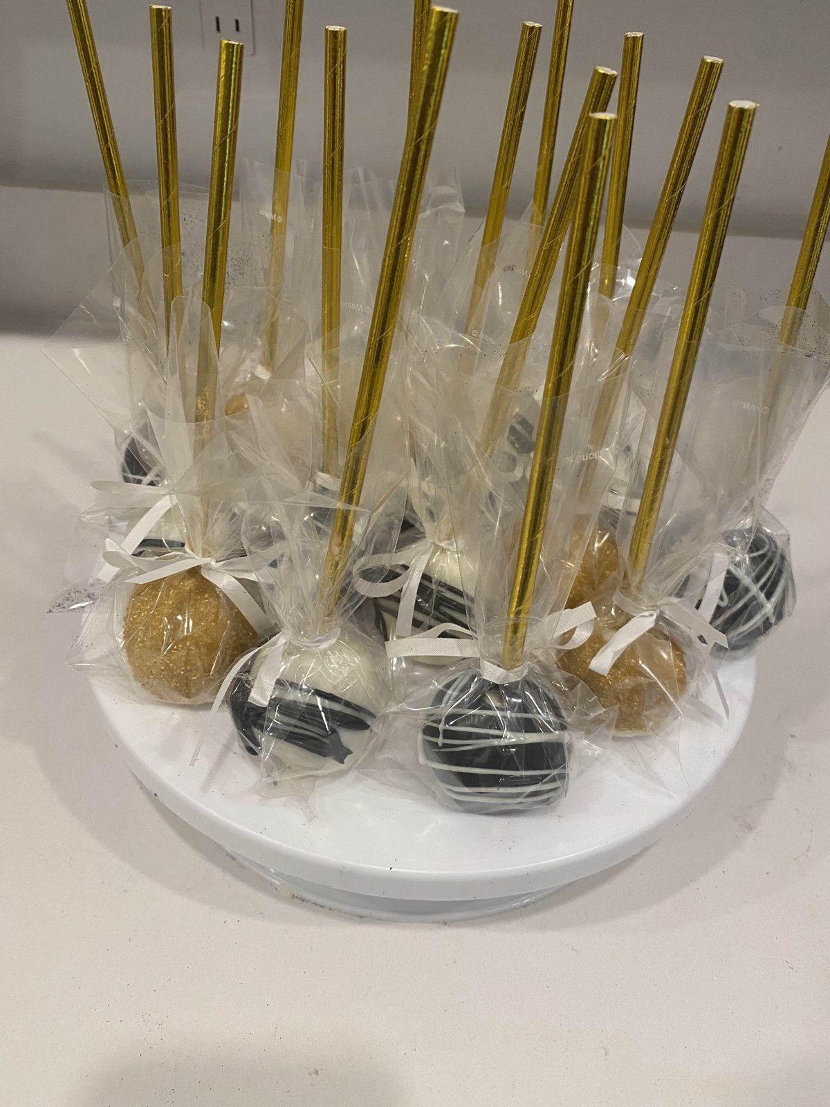Cake pops in gold, white, and black, wrapped in clear bags with gold sticks.