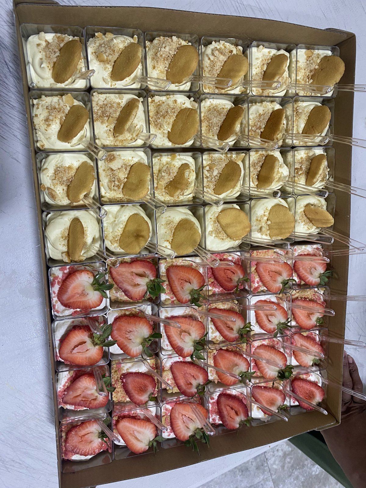 Tray of dessert cups: vanilla cream cups topped with cookies, and strawberry cream cups topped with fresh strawberry slices.