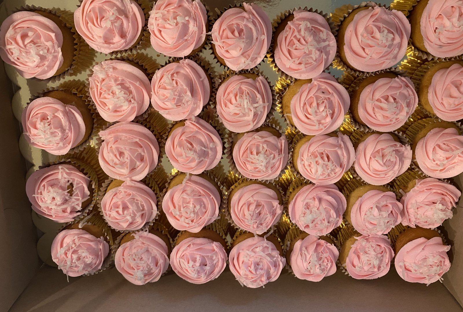 Box of cupcakes piped with pink buttercream roses and sprinkles.